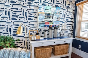A kitchen with a white cabinet, wicker baskets, a coffee station, and a wall with a whale pattern.