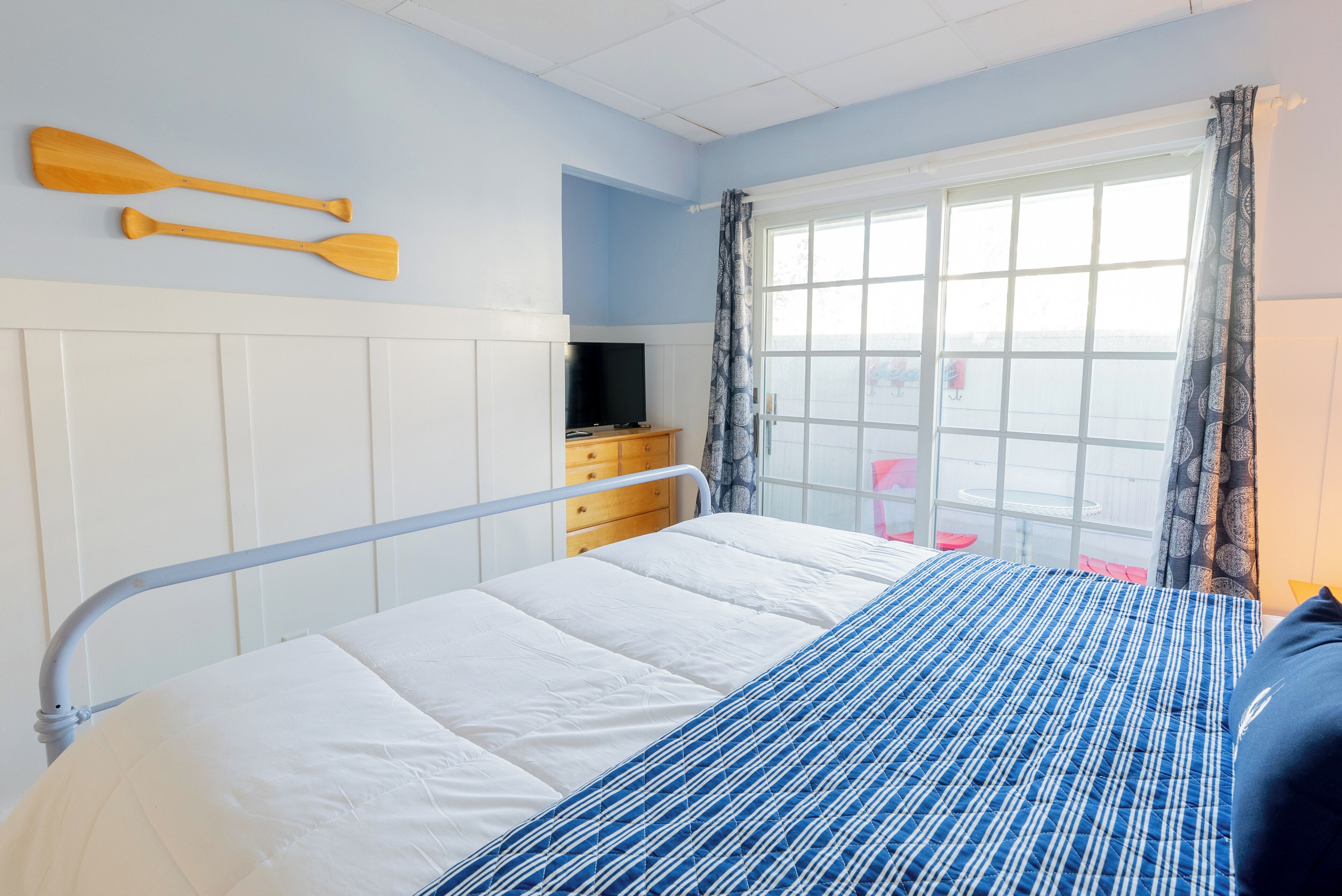 A bedroom with a bed, a dresser, a television, and a window with curtains.