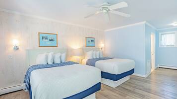 A bedroom with two beds, a ceiling fan, and framed pictures on the wall.