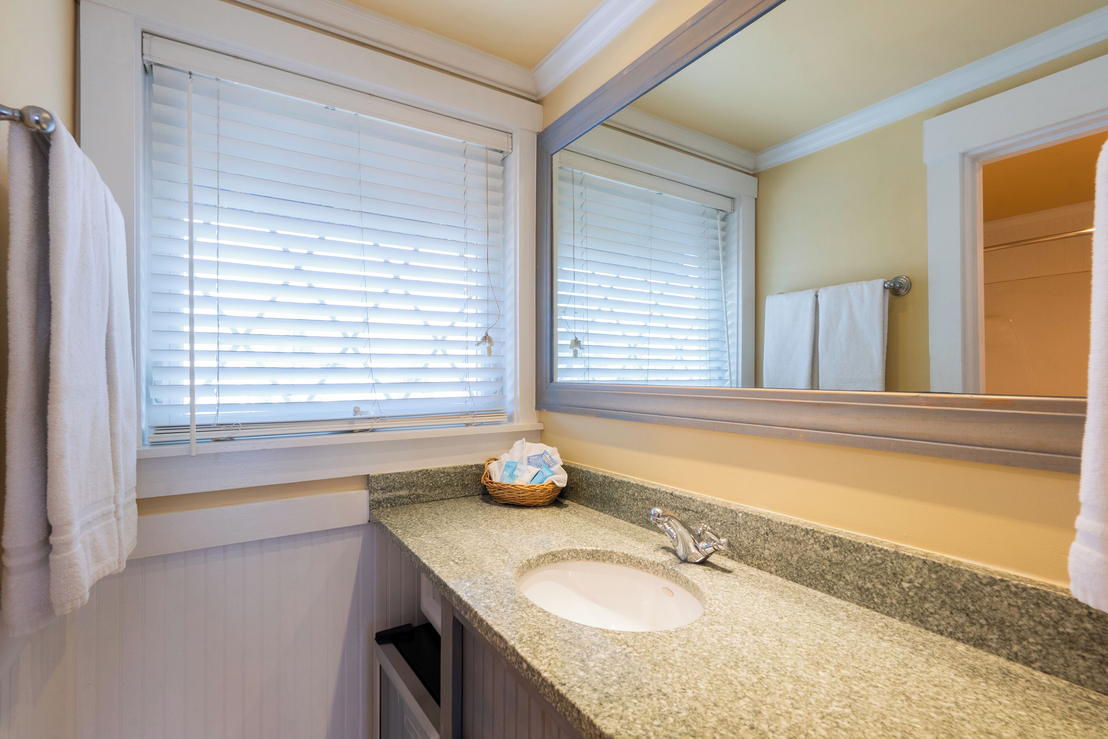 A bathroom with a granite countertop sink, a mirror, and a window with blinds.