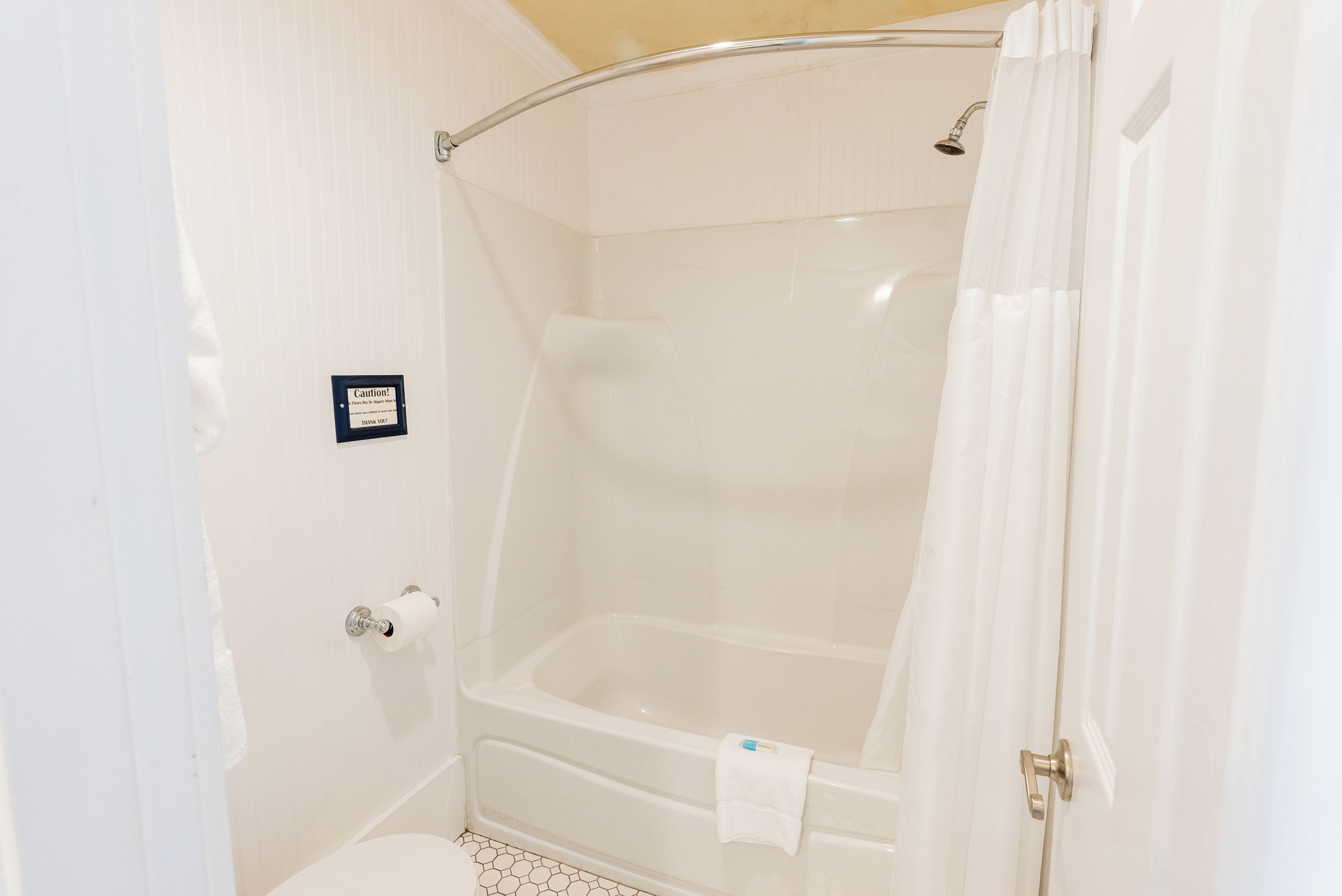 A bathroom with a shower, toilet, and a caution sign on the wall.