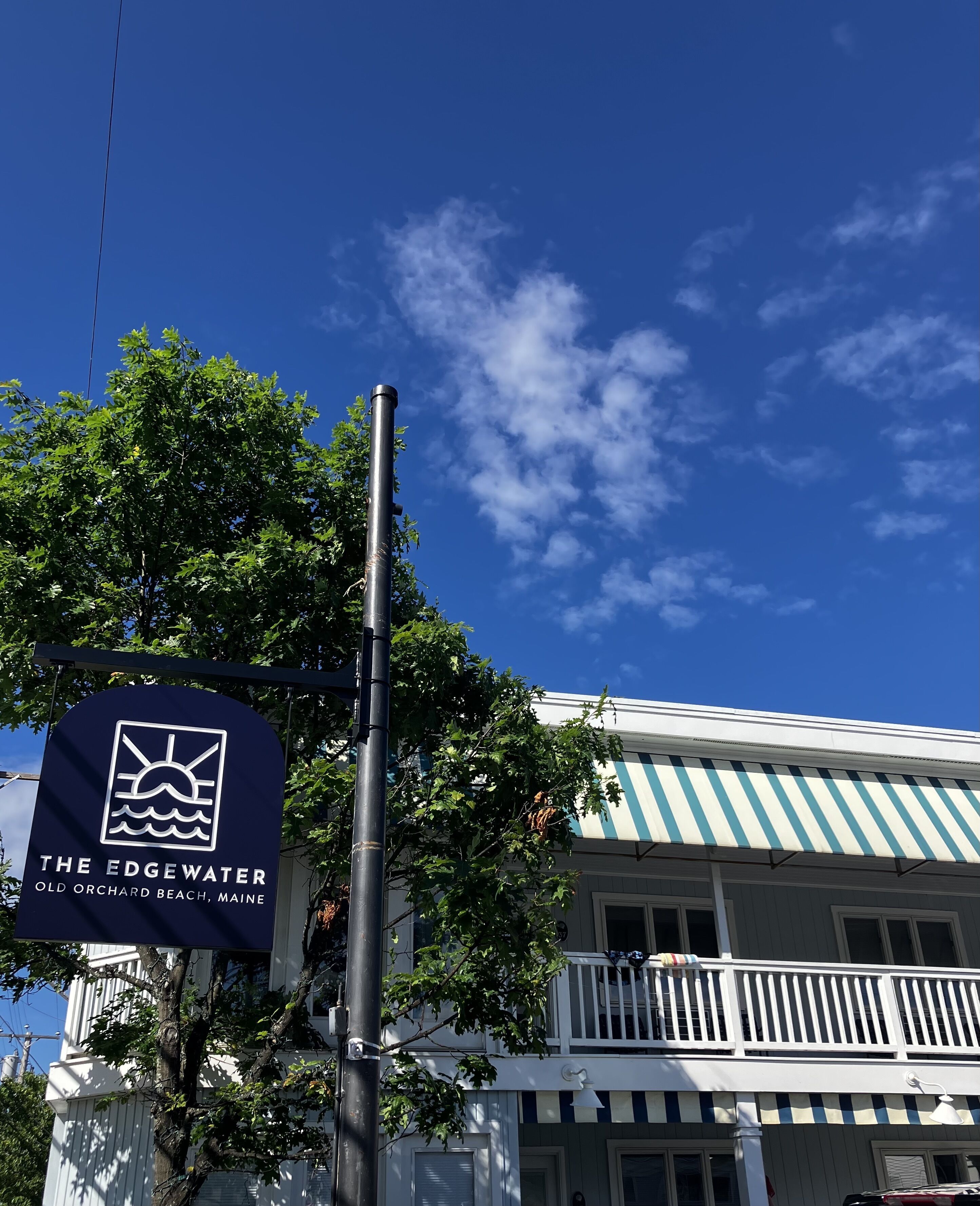 A sign for The Edgewater in Old Orchard Beach, Maine, with a clear blue sky and a building with a striped awning.