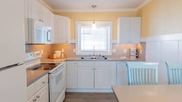 A kitchen with white cabinets, a stainless steel refrigerator, a microwave, a stove, and a sink.