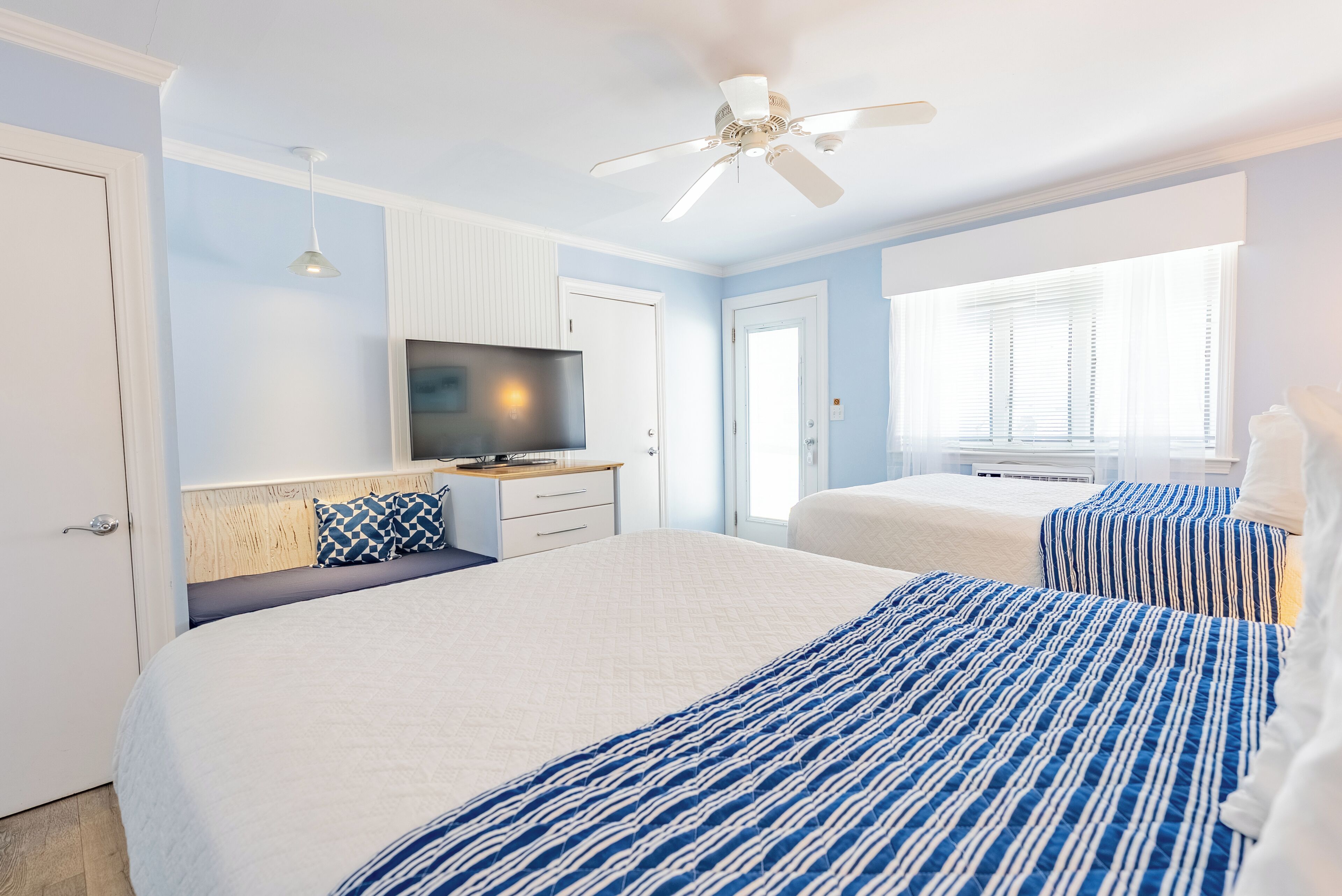 A bedroom with two beds, a ceiling fan, a TV, and a window with blinds.