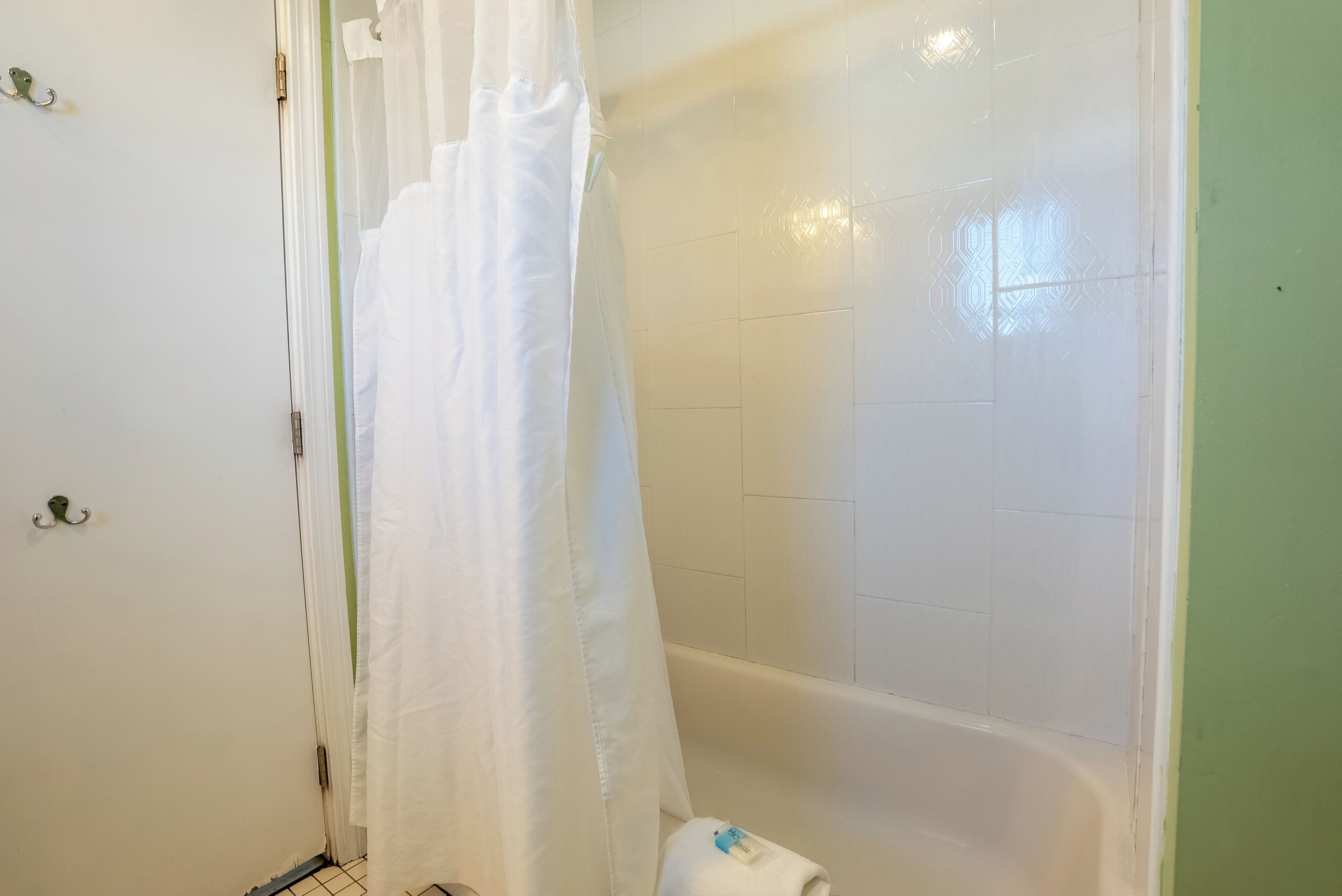 A bathroom with a bathtub, a white shower curtain, and a towel on the floor.