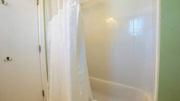 A bathroom with a bathtub, a white shower curtain, and a towel on the floor.