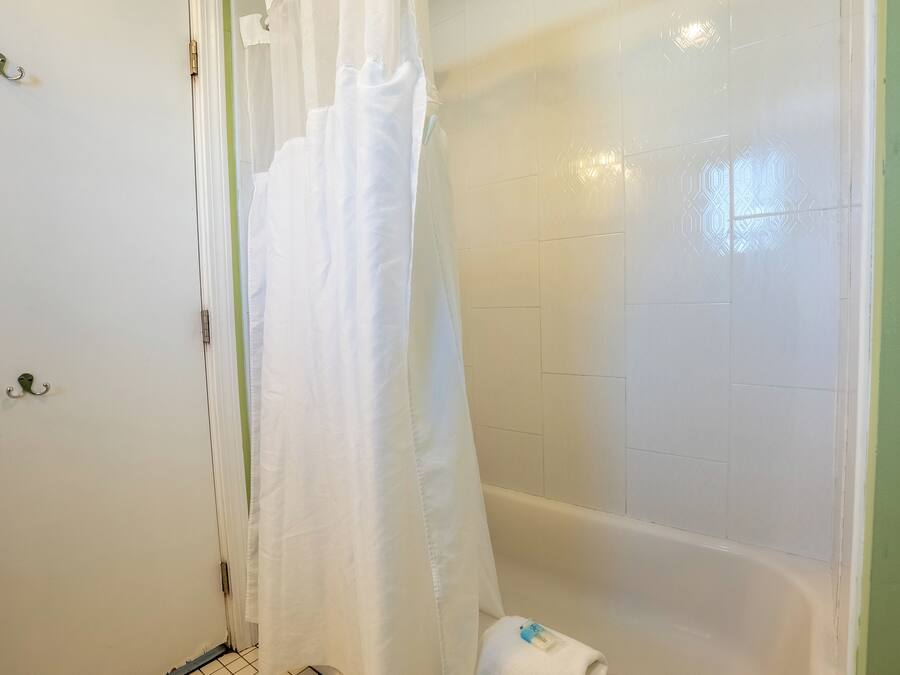 A bathroom with a bathtub, a white shower curtain, and a towel on the floor.