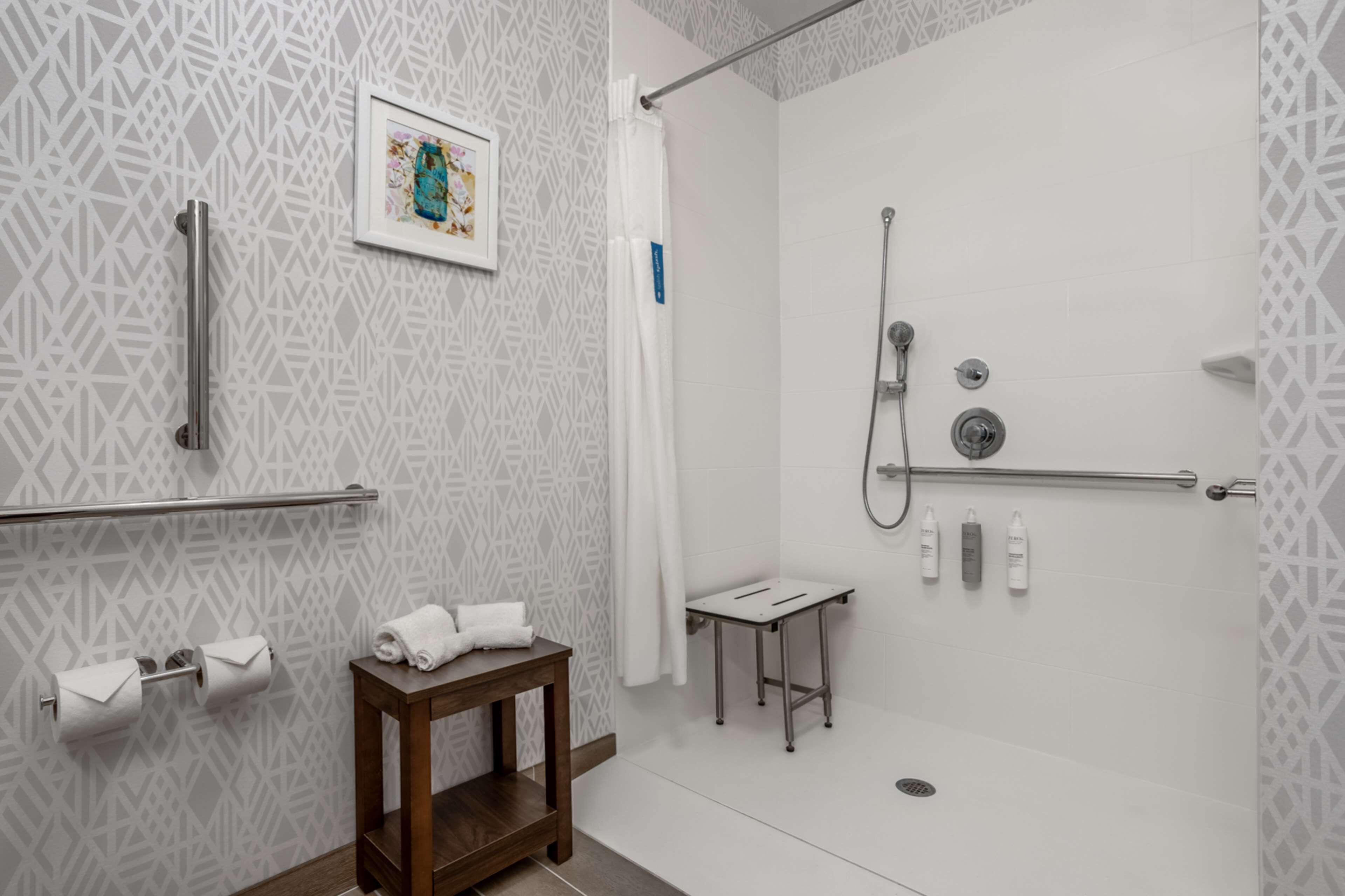 Un baño moderno con ducha, papel higiénico, una toalla y una mesita.