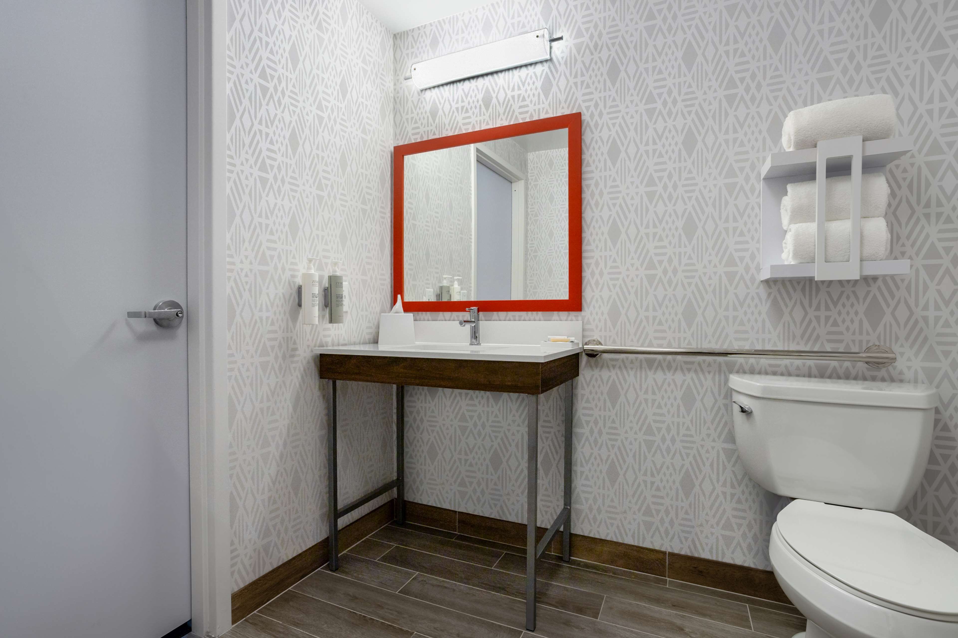 A bathroom with a patterned wall, a white toilet, a mirror with a red frame, and a towel rack.