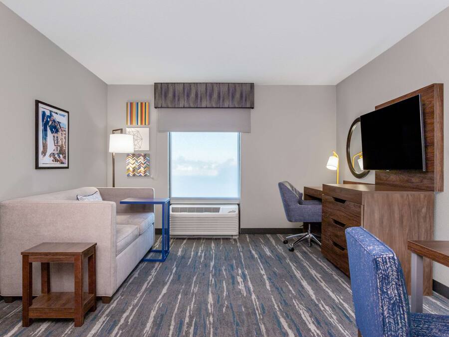 A hotel room with a sofa, a desk, a chair, a television, and a window with a view.