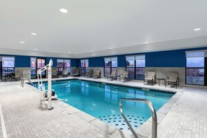 Una piscina interior con vistas despejadas a la ciudad a través de amplias ventanas, un área de descanso junto a la piscina y un puesto de socorristas.