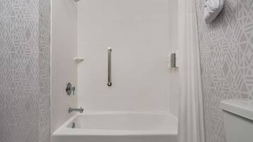 A bathroom with a white bathtub, a showerhead, a grab bar, and a toilet with a towel hanging on the wall.