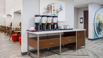 A modern hotel lobby with a coffee station, seating area, and artwork on the walls.