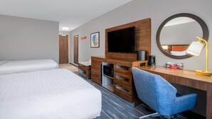 Une chambre d’hôtel avec deux lits, un bureau avec une télévision, un miroir, une chaise et un four à micro-ondes.