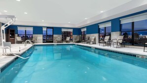 Une piscine intérieure moderne, avec une eau d’un bleu limpide, entourée de chaises longues et d’un bar au bord de la piscine.