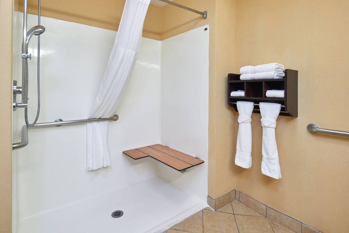 A shower area with a glass door, a towel rack with folded towels, and a wooden shelf.