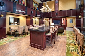 A spacious hotel lobby with a central bar, multiple seating areas, and a large chandelier.