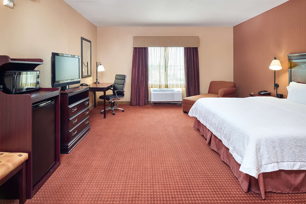 A hotel room with a bed, a desk with a computer, a chair, a television, and an air conditioning unit.