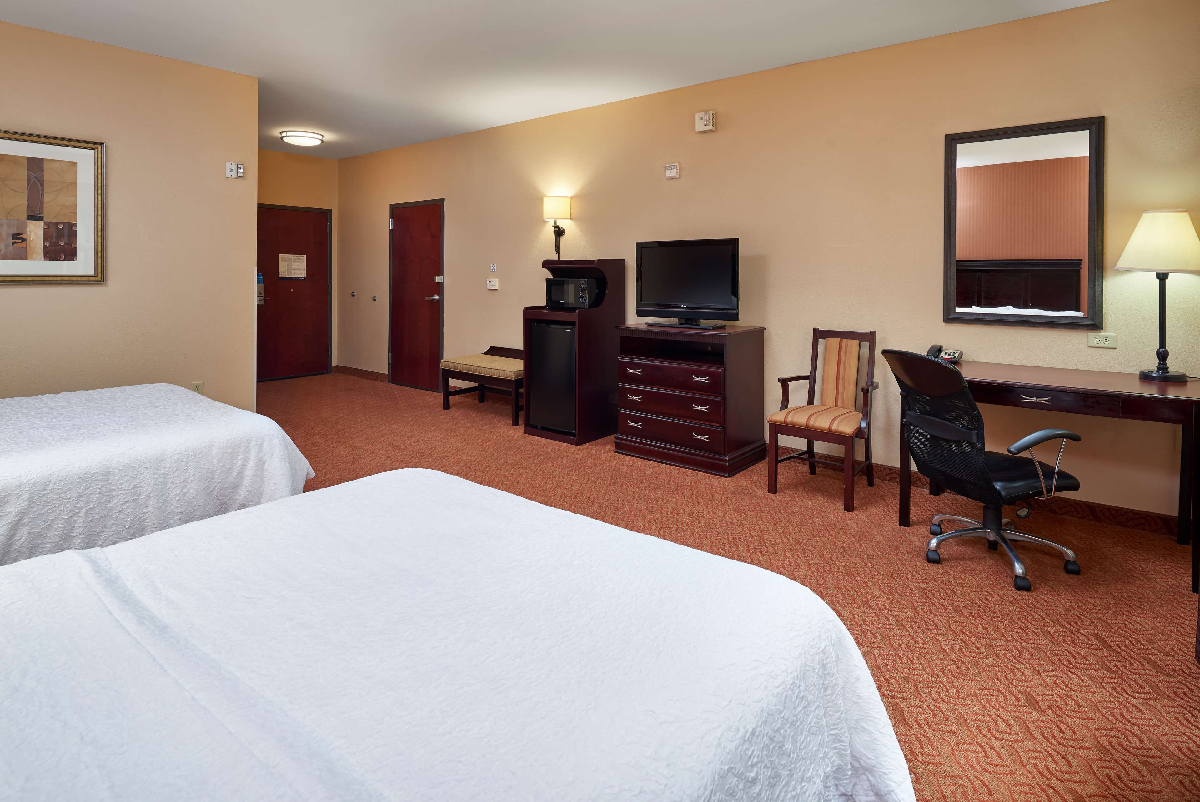 Une chambre d’hôtel avec deux lits, un bureau avec une chaise, une télévision, une commode et un miroir.