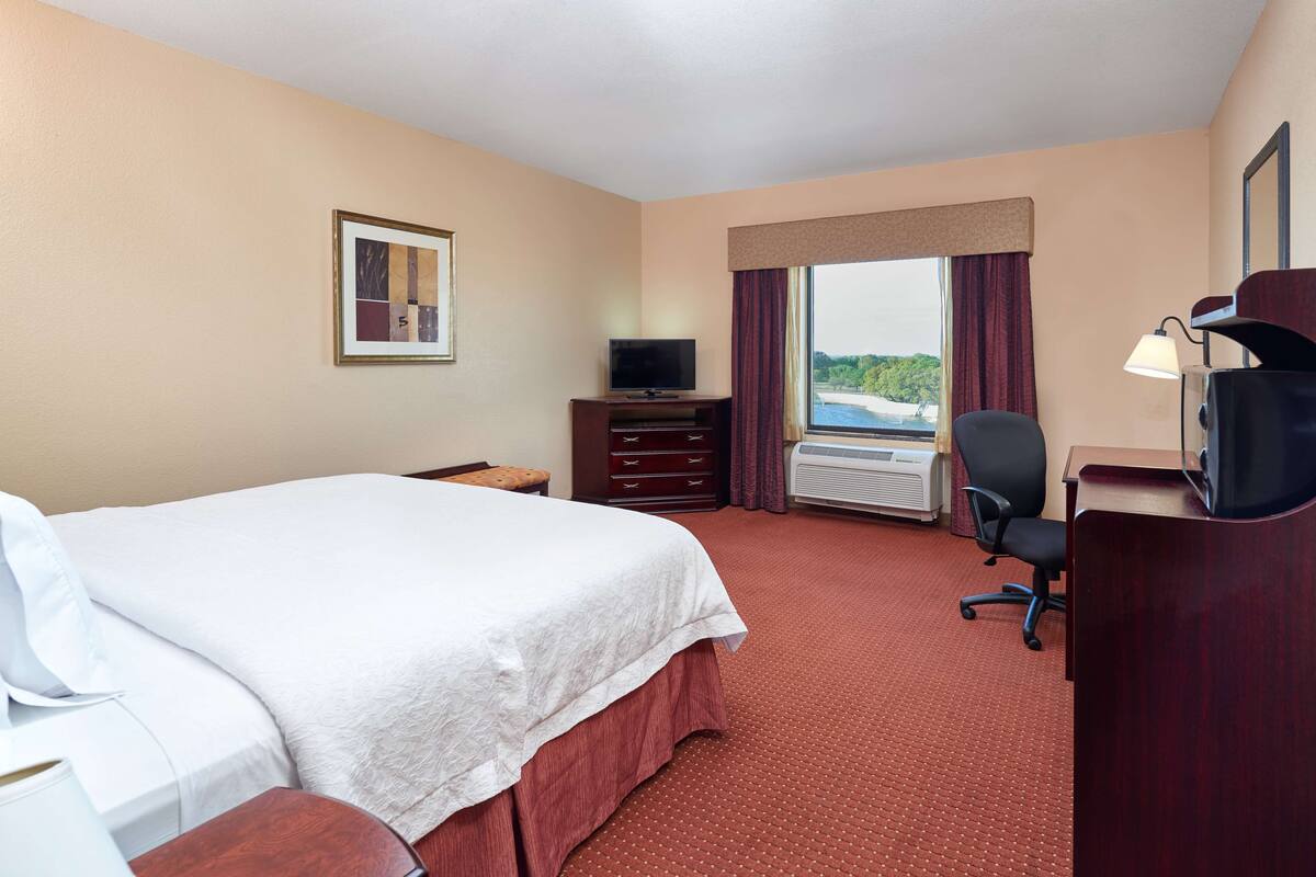 A hotel room with a large bed, a desk, a chair, a television, and a window with a view of the outdoors.