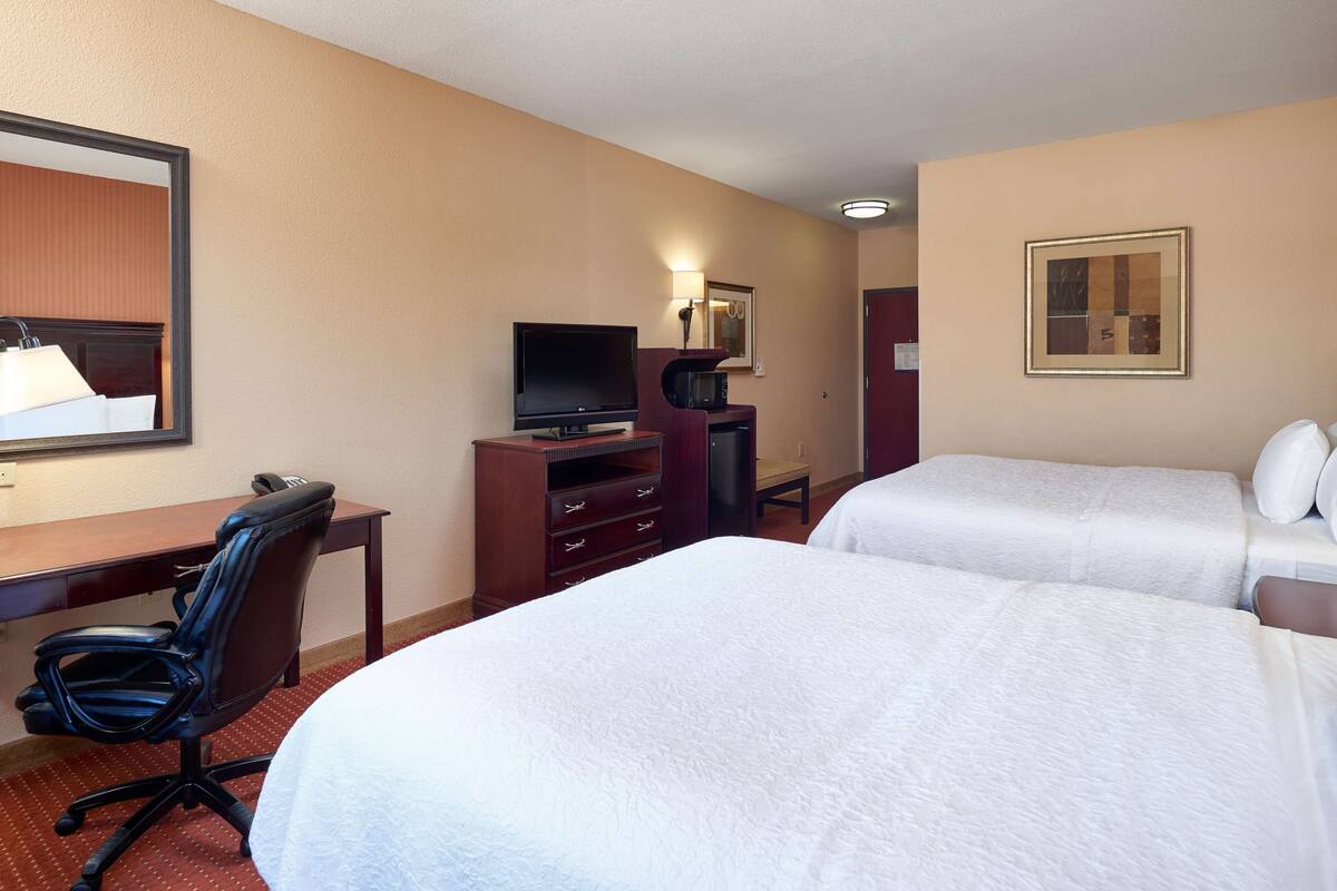 A hotel room with two beds, a desk with a computer, a chair, a TV, and a microwave.