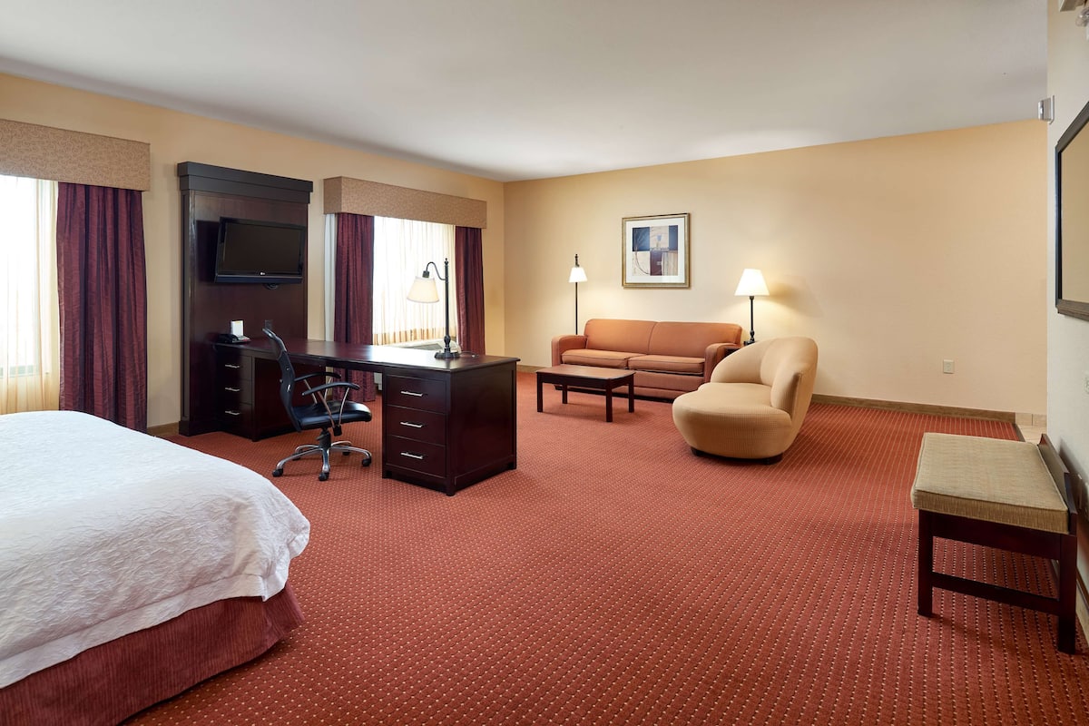 A hotel room with a bed, a desk with a chair, a sofa, a small table, and a TV mounted on the wall.