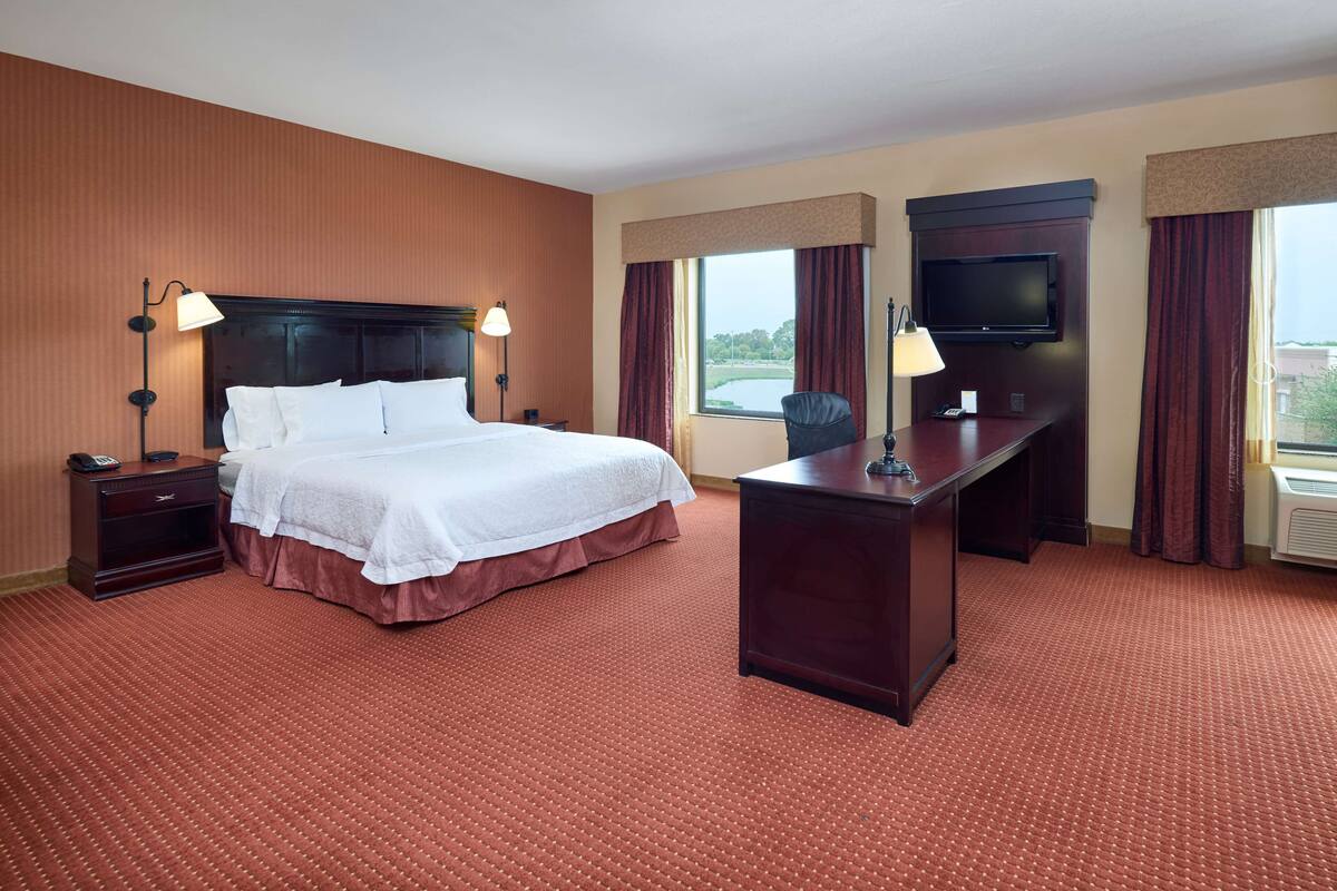 A hotel room with a large bed, a desk, a TV, and a view of the outdoors.
