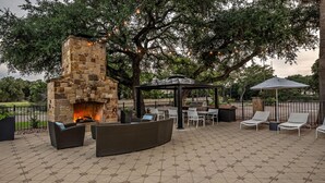 An outdoor patio with a stone fireplace, wicker furniture, a gazebo, and string lights. - Hampton Inn & Suites Boerne (Boerne)