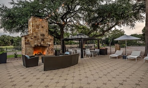An outdoor patio with a stone fireplace, wicker furniture, a gazebo, and string lights. - Hampton Inn & Suites Boerne (Boerne)