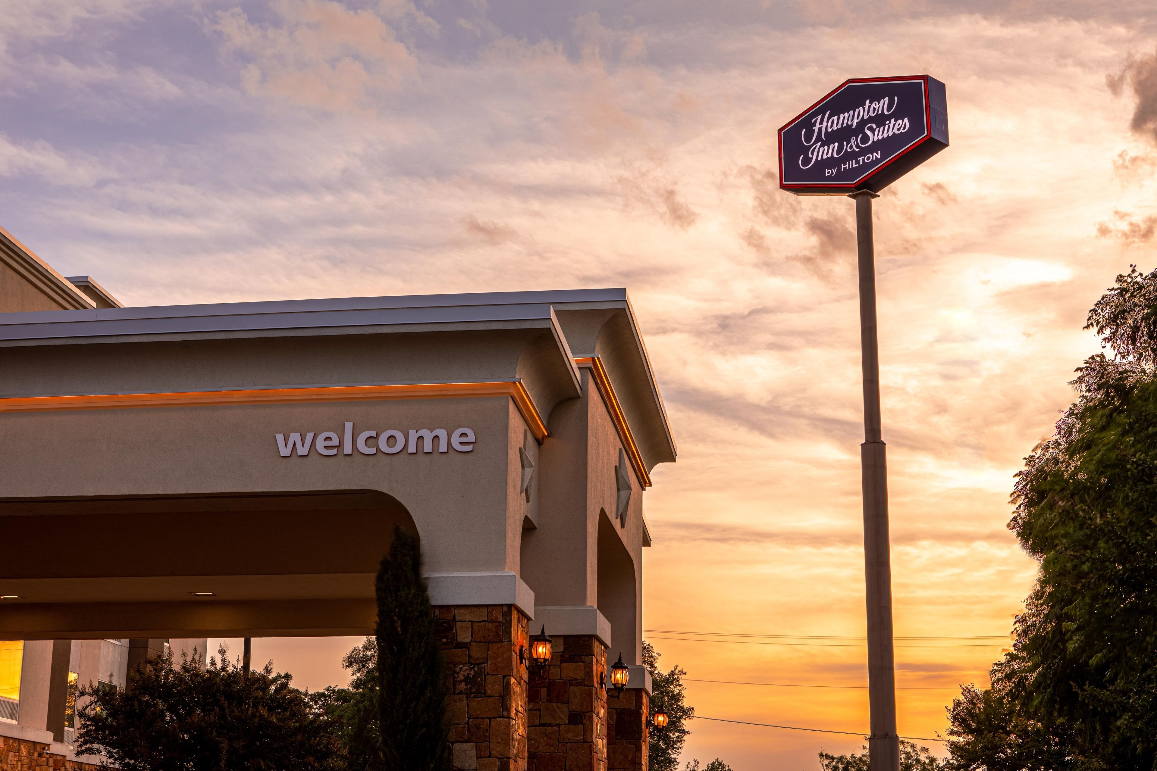 A hotel entrance with a 'Welcome' sign and a 'Hampton Inn & Suites by Hilton' sign.