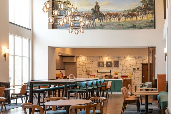 Un restaurante espacioso con un alto techo, una zona de bar central y un mural de un vaquero a caballo.