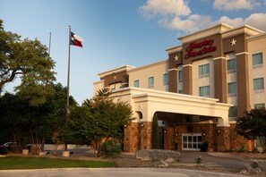 A Hampton Inn & Suites building with a flagpole, stone facade, and a clear sky. - Hampton Inn & Suites Boerne (Boerne)