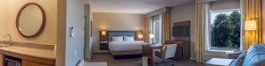 A hotel room with a bed, desk, chair, and a large window with a view of trees. - Hampton Inn & Suites Boerne (Boerne)