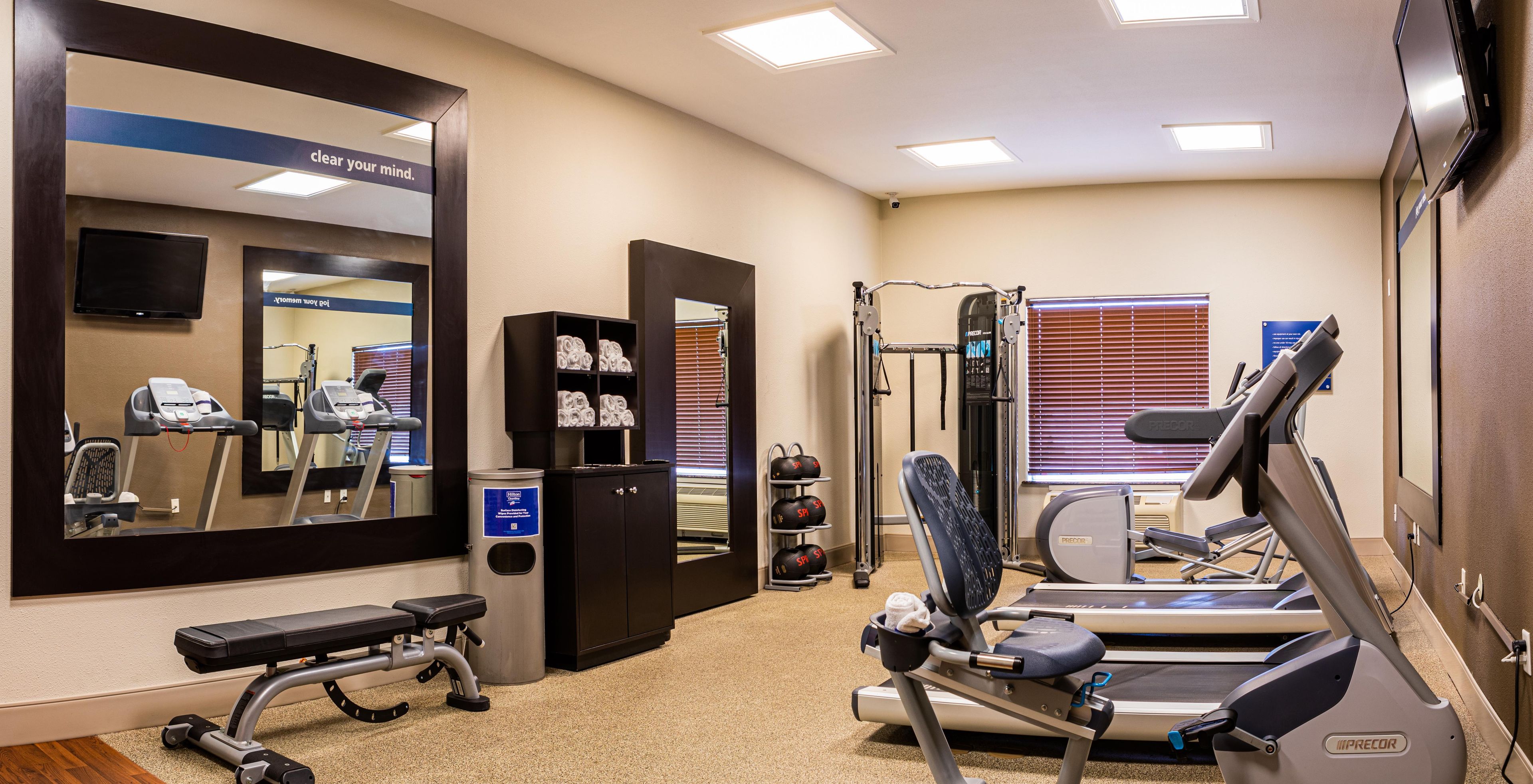 A gym with exercise equipment, a bench, a mirror, and a wall-mounted TV.