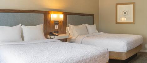 A hotel room with two beds, a bedside table with a lamp, a phone, and a framed picture on the wall.
