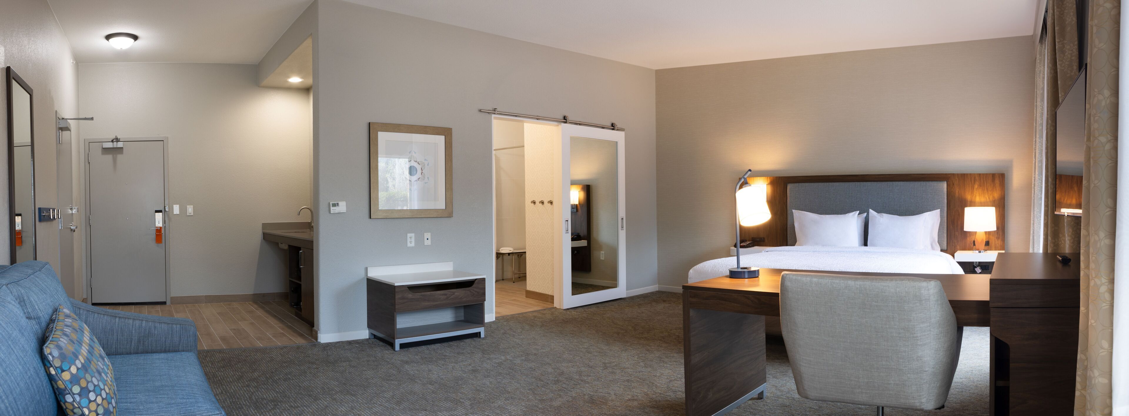 A hotel room with a bed, desk, chair, and a small seating area with a sofa.