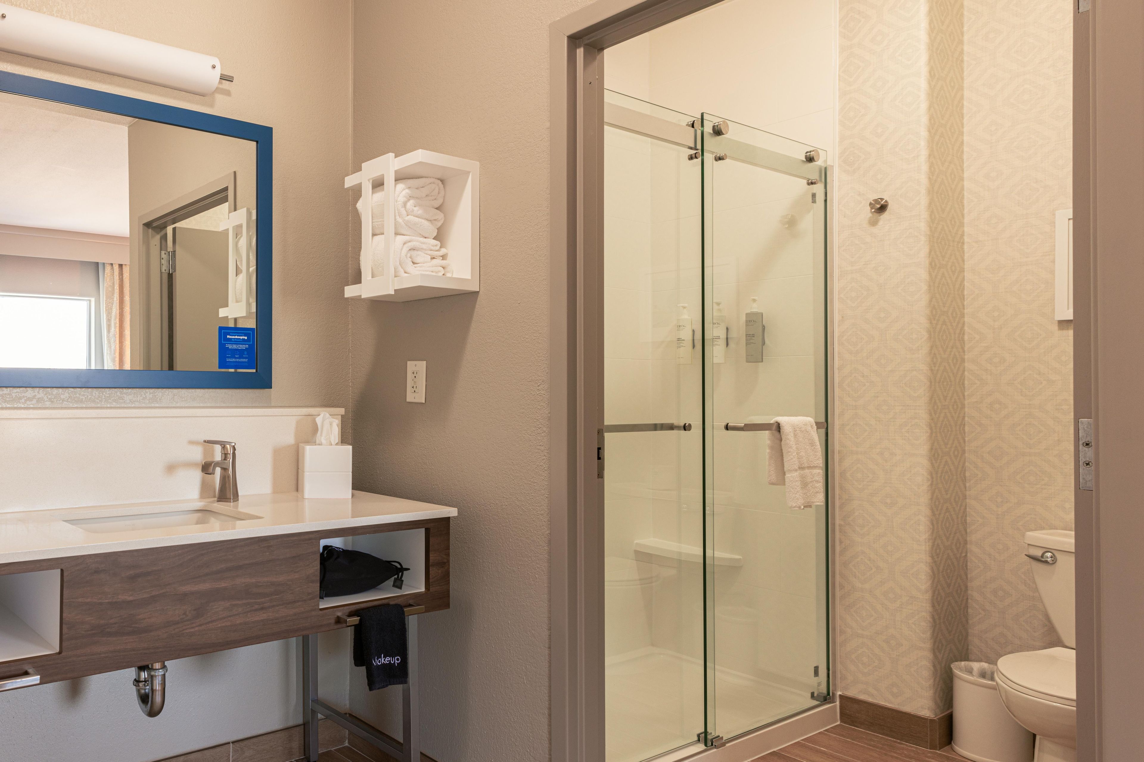 A modern bathroom with a glass shower enclosure, a wooden vanity, and a mirror with a blue frame.