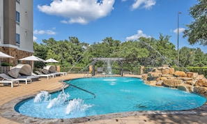 A swimming pool with a waterfall feature, lounge chairs, and a stone wall.