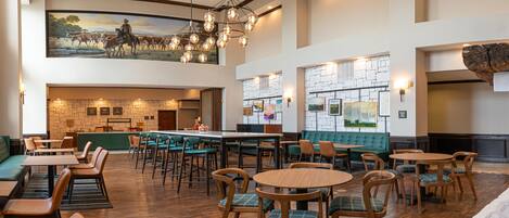 A spacious restaurant with high ceilings, a bar area, and a mural of a cowboy on horseback.
