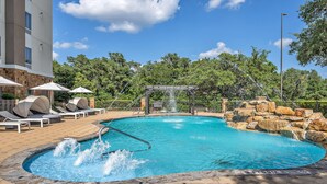 A swimming pool with a waterfall feature, lounge chairs, and a stone wall. - Hampton Inn & Suites Boerne (Boerne)