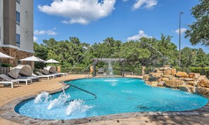 A swimming pool with a waterfall feature, lounge chairs, and a stone wall. - Hampton Inn & Suites Boerne (Boerne)
