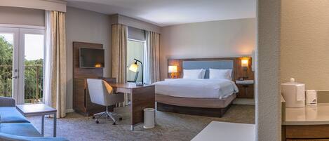 A hotel room with a bed, desk, chair, and a bathroom with a sink and mirror.