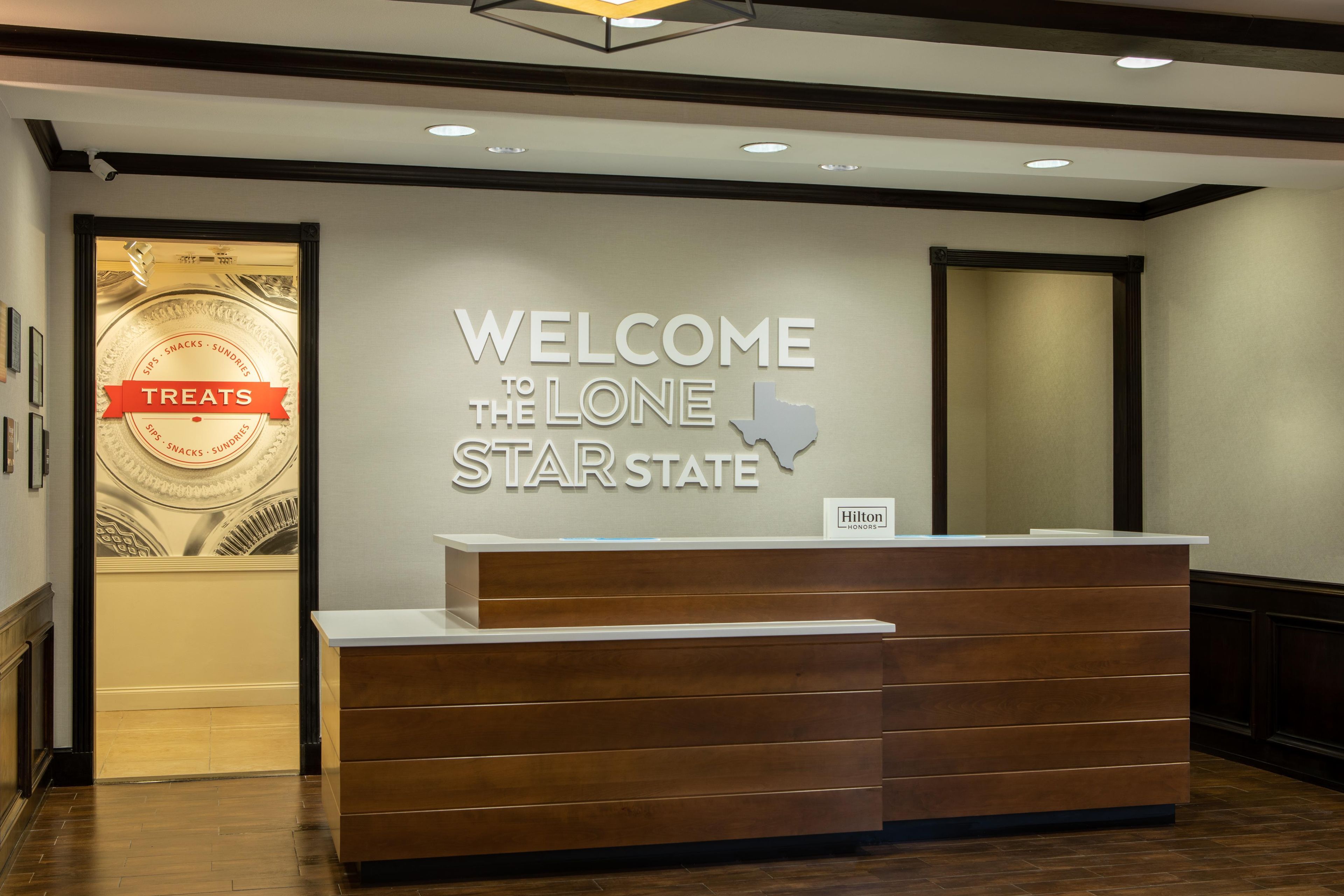 Un mostrador de recepción de hotel con un cartel que dice 'BIENVENIDOS AL ESTADO DE LA ESTRELLA SOLITARIA' y una placa de 'Hilton Honors'.