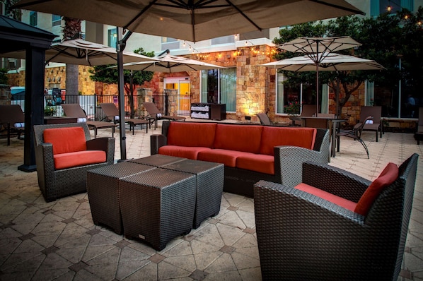 An outdoor patio area with wicker furniture, including sofas and chairs, under large umbrellas. - Hampton Inn & Suites Boerne (Boerne)