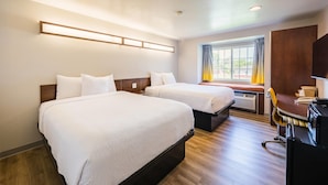 A hotel room with two beds, a desk, and a window with curtains.