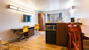 A compact kitchen with a microwave, a small refrigerator, a wooden dining table, and a yellow office chair.