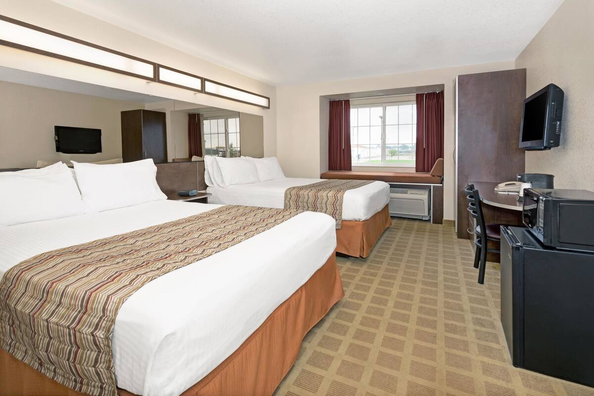 A hotel room with two beds, a desk, a television, and a window with curtains.
