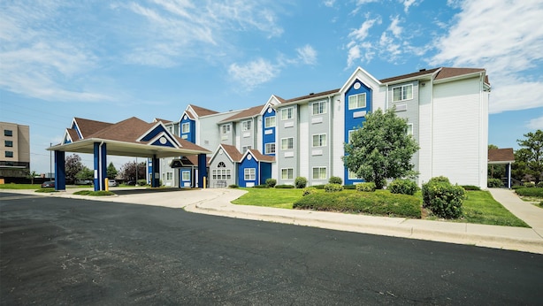 A multi-story hotel with a covered parking area, a well-maintained lawn, and a clear sky.