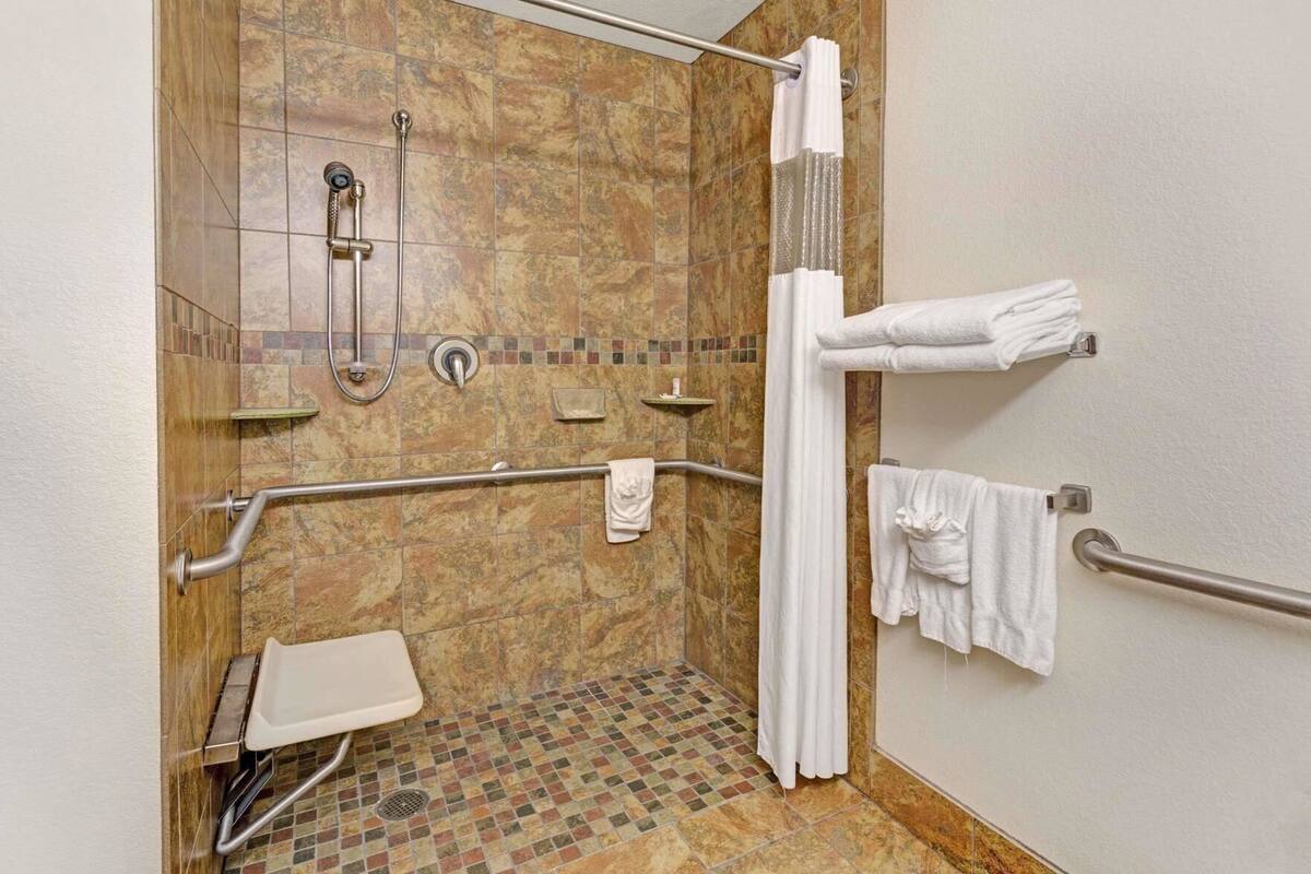 A handicap-accessible shower with grab bars, a white sink, and a tiled floor.