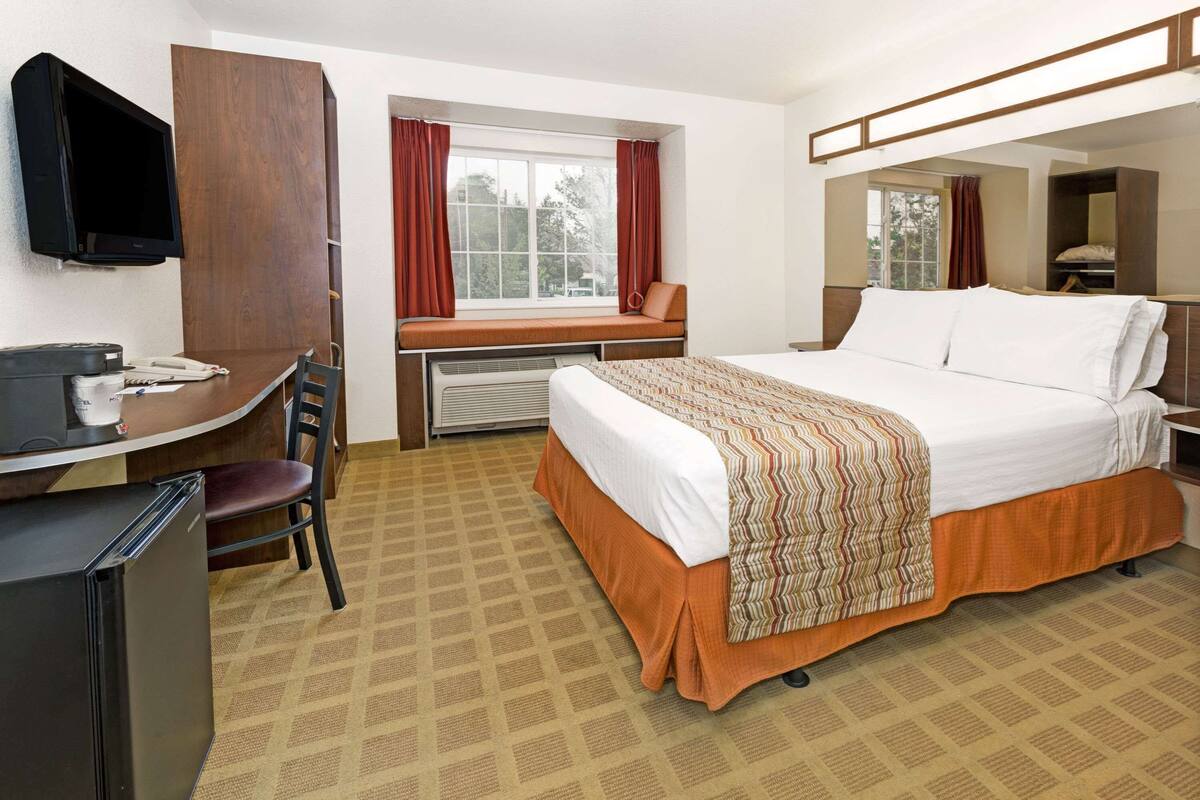 A hotel room with a bed, a desk with a chair, a television, and a window with curtains.